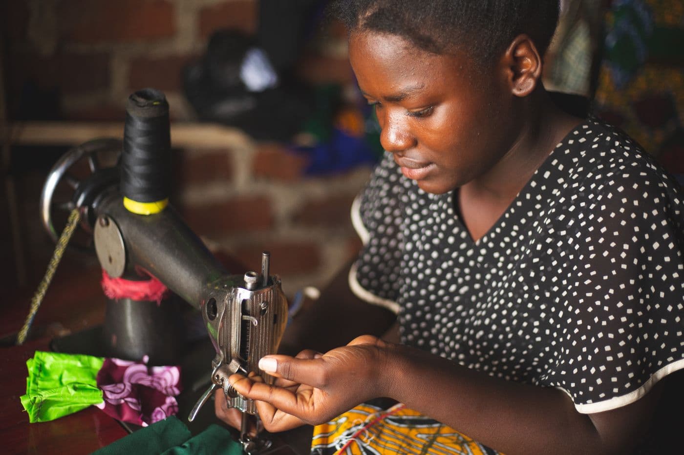 A young seamstress focused on sewing in a Ugandan workshop