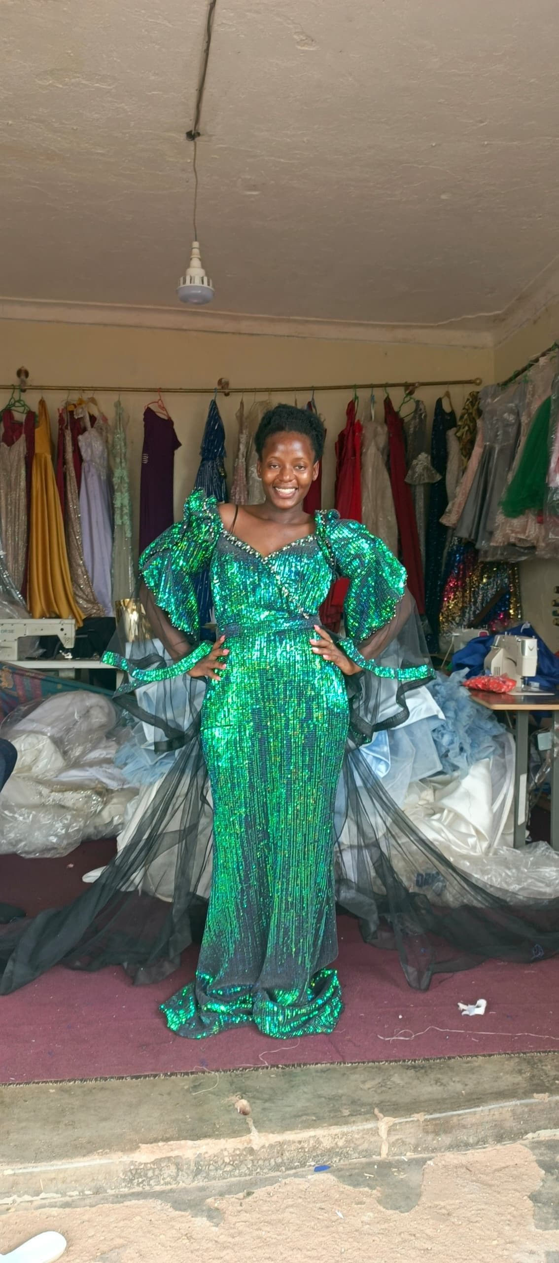 A model smiling in a sequined emerald gown backstage at a fashion show