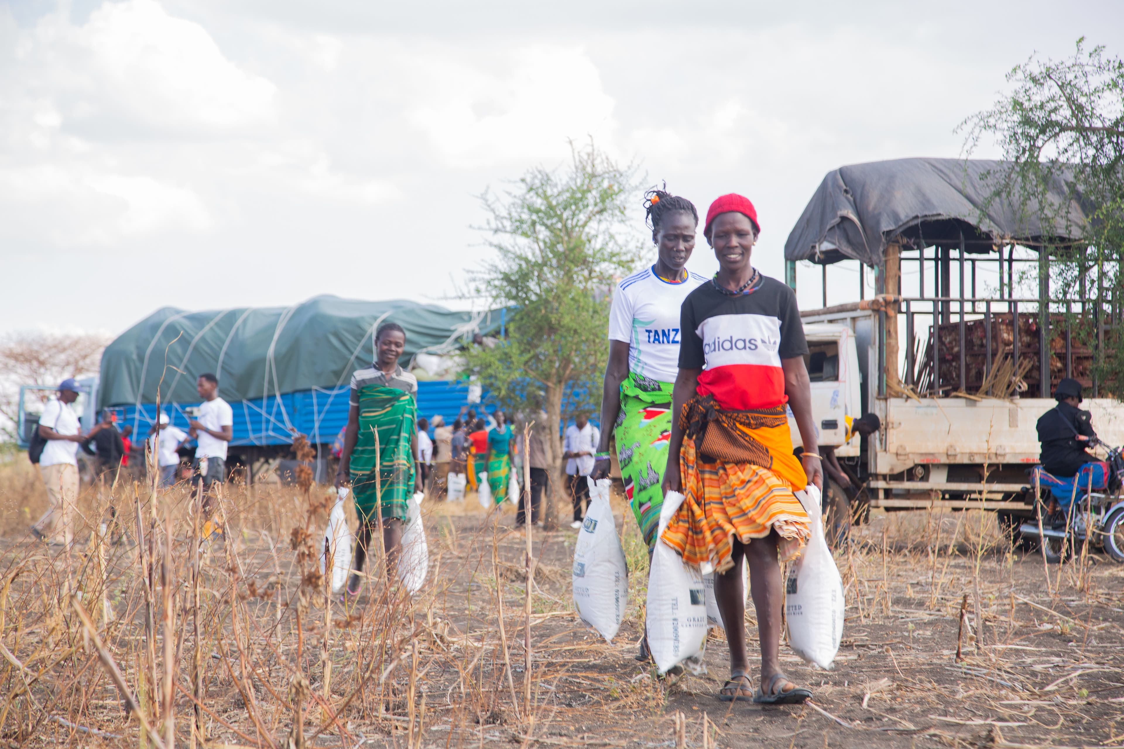 Women carrying sacks of food aid away from a relief distribution truck in rural Uganda