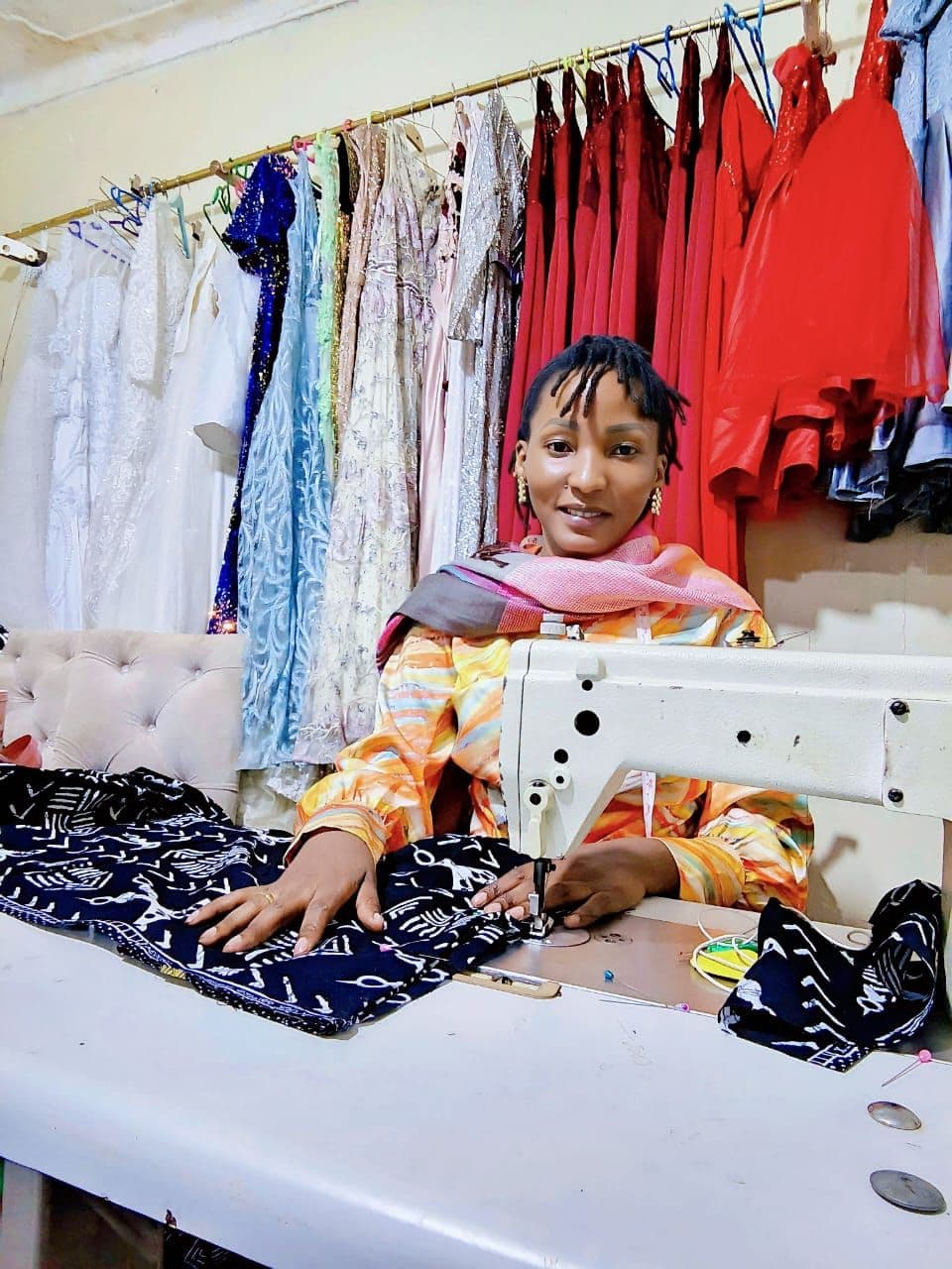 A tailor at her sewing machine surrounded by finished garments