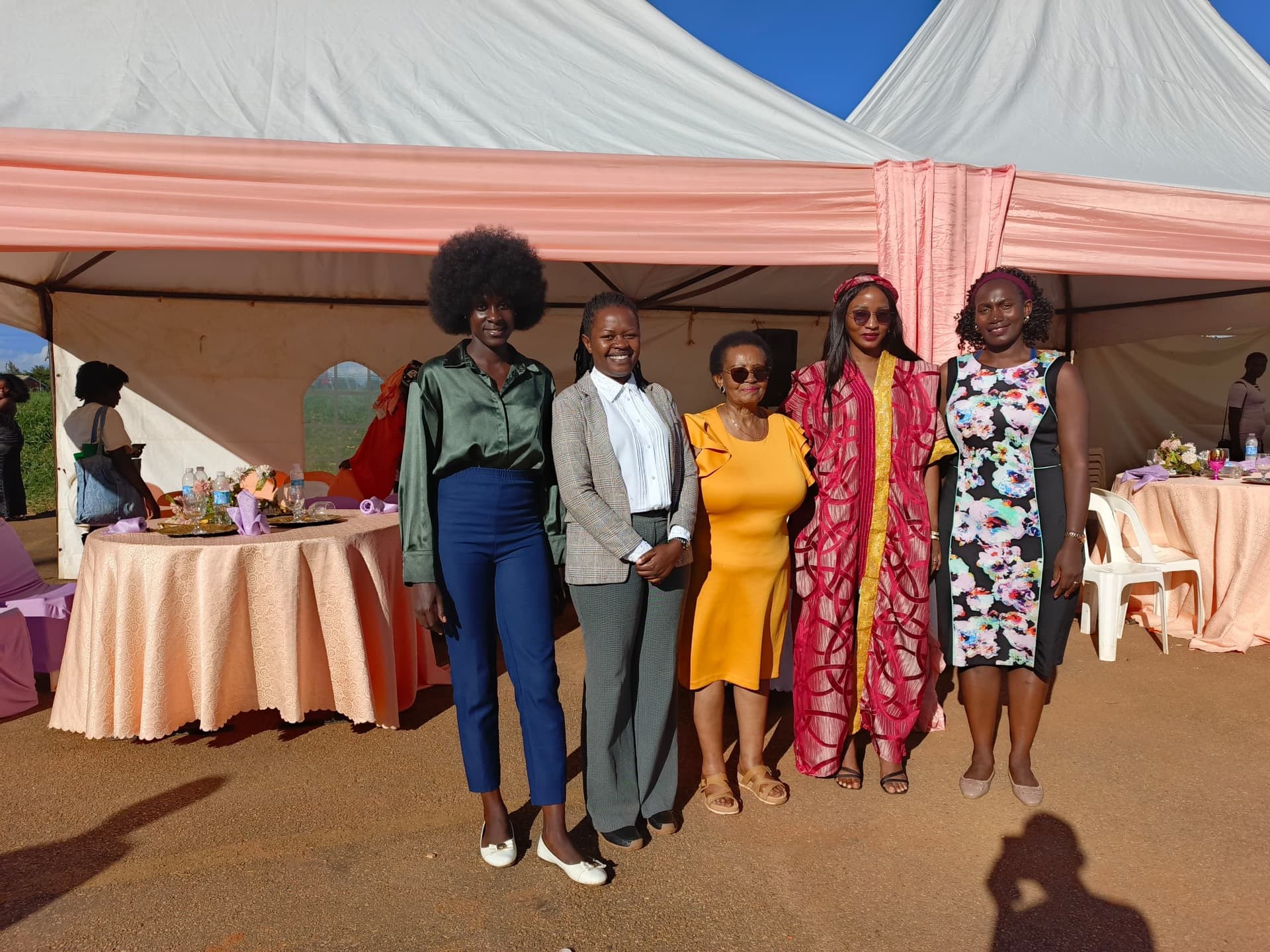 Five women posing together at an outdoor community event